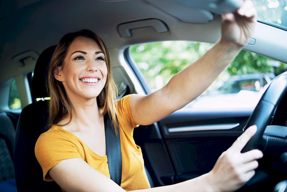 Car interior view of female woman driver adjusting mirrors before driving a car.