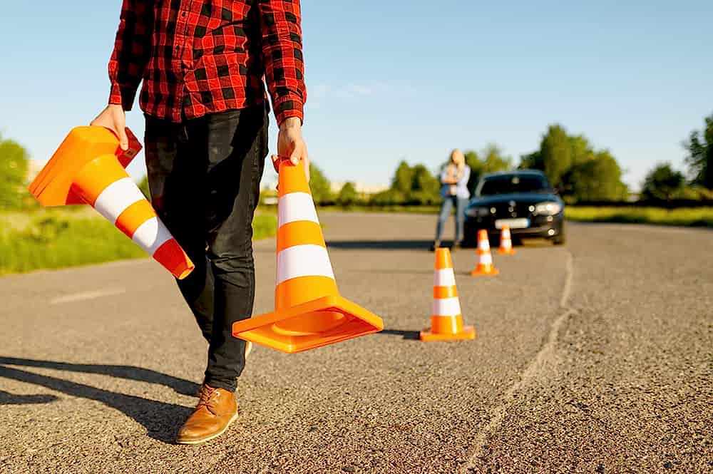 Male instructor puts traffic cones on road, driving school. Man teaching lady to drive vehicle. Driver's license education
